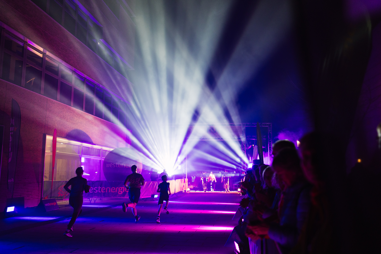 Lichtshow in Violett und Blau über dem Startbereich, Läufer laufen durch die Lichtstrahlen