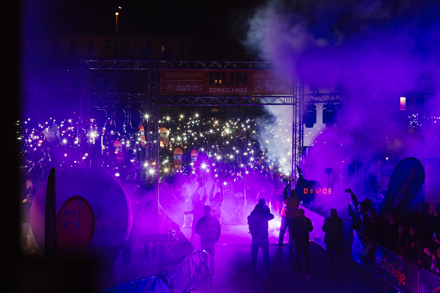 Startbereich des RUNschnellweg in violettem Licht und Nebel, tausende leuchtende Stirnlampen unter dem Startbogen